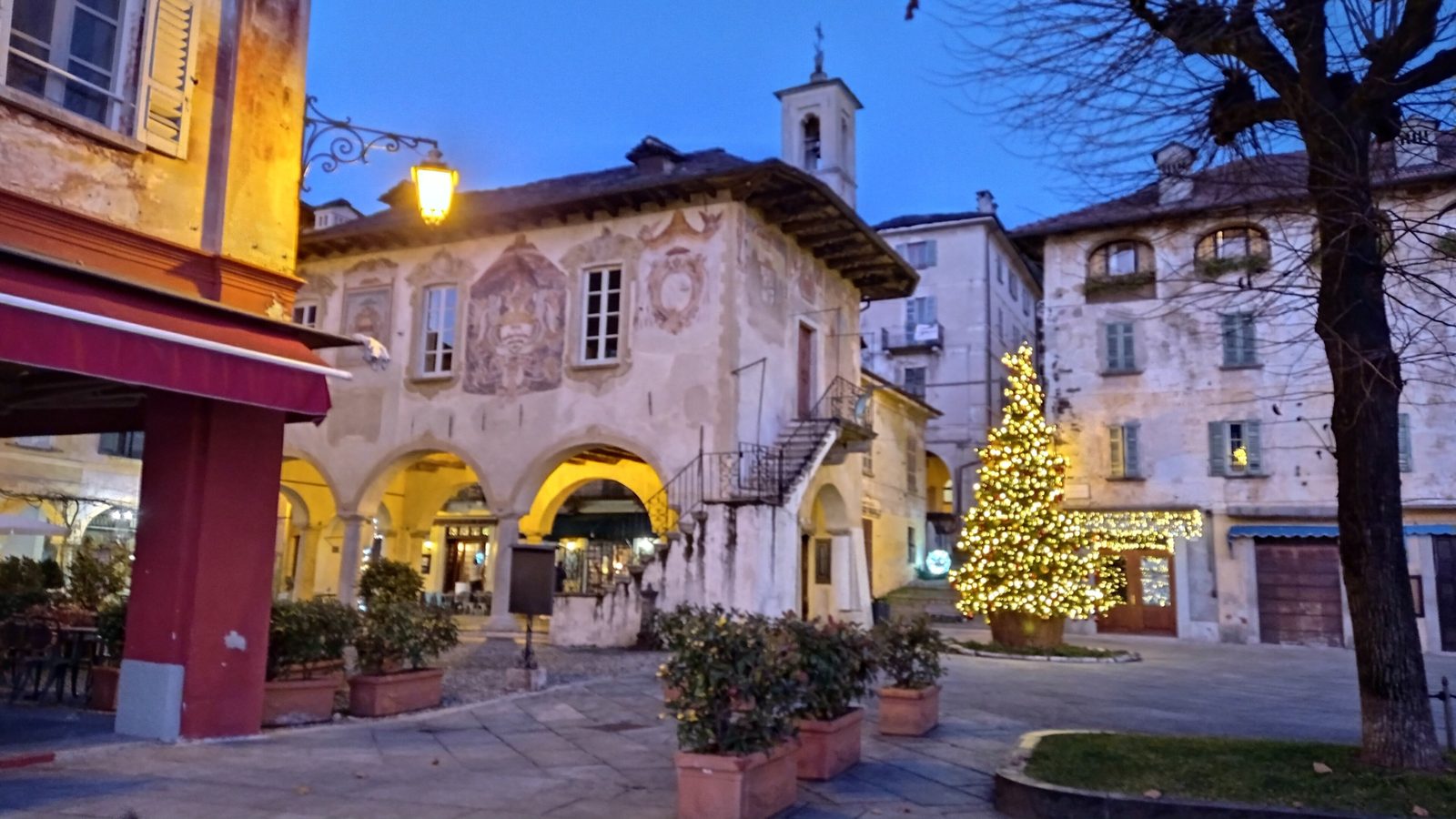 Piazza Motta a Orta San Giulio al crepuscolo in dicembre, con il Palazzo della Comunità affrescato e l'albero di Natale illuminato