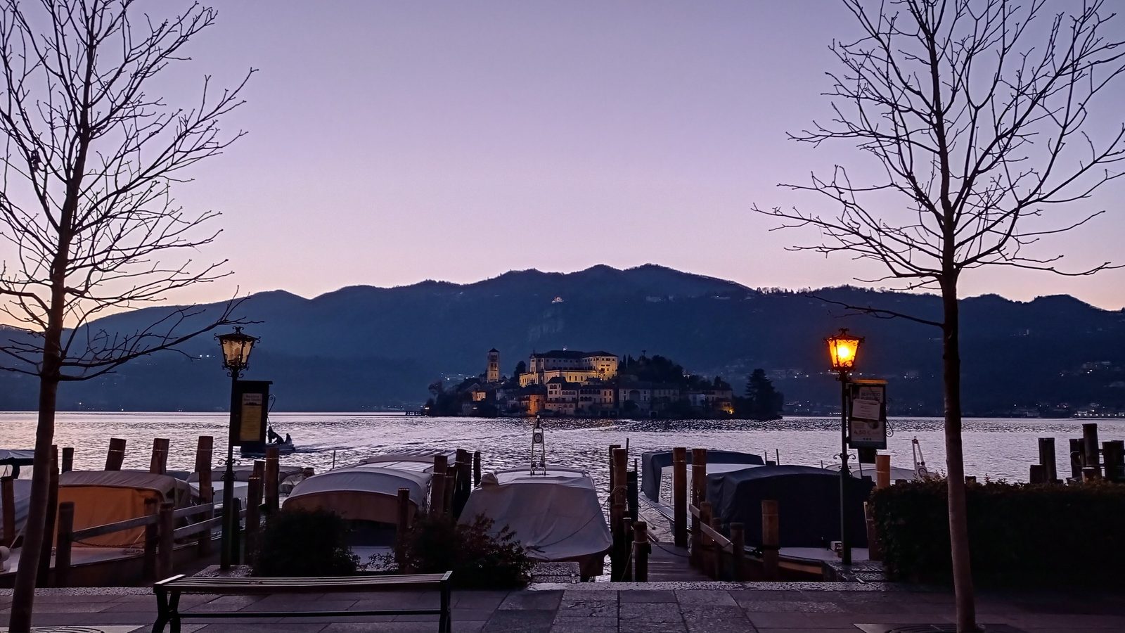 L'Isola San Giulio al crepuscolo d'inverno vista dal lungolago di Orta San Giulio, tra alberi spogli e lampioni accesi