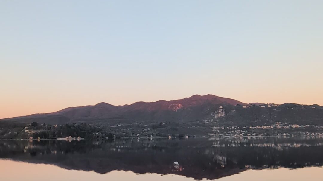 Lake Orta at dawn in April, mountains perfectly reflected in the glass-flat water