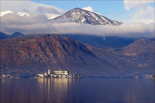 Lake Orta in winter with snow-capped mountains reflected in the clear water and San Giulio Island in the distance