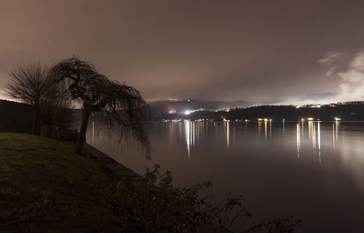 Der Ortasee bei Nacht, die Lichter der Dörfer spiegeln sich im Wasser.